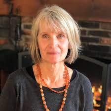  Judith Bird in front of a fireplace with a grey / black shirt and orange beads