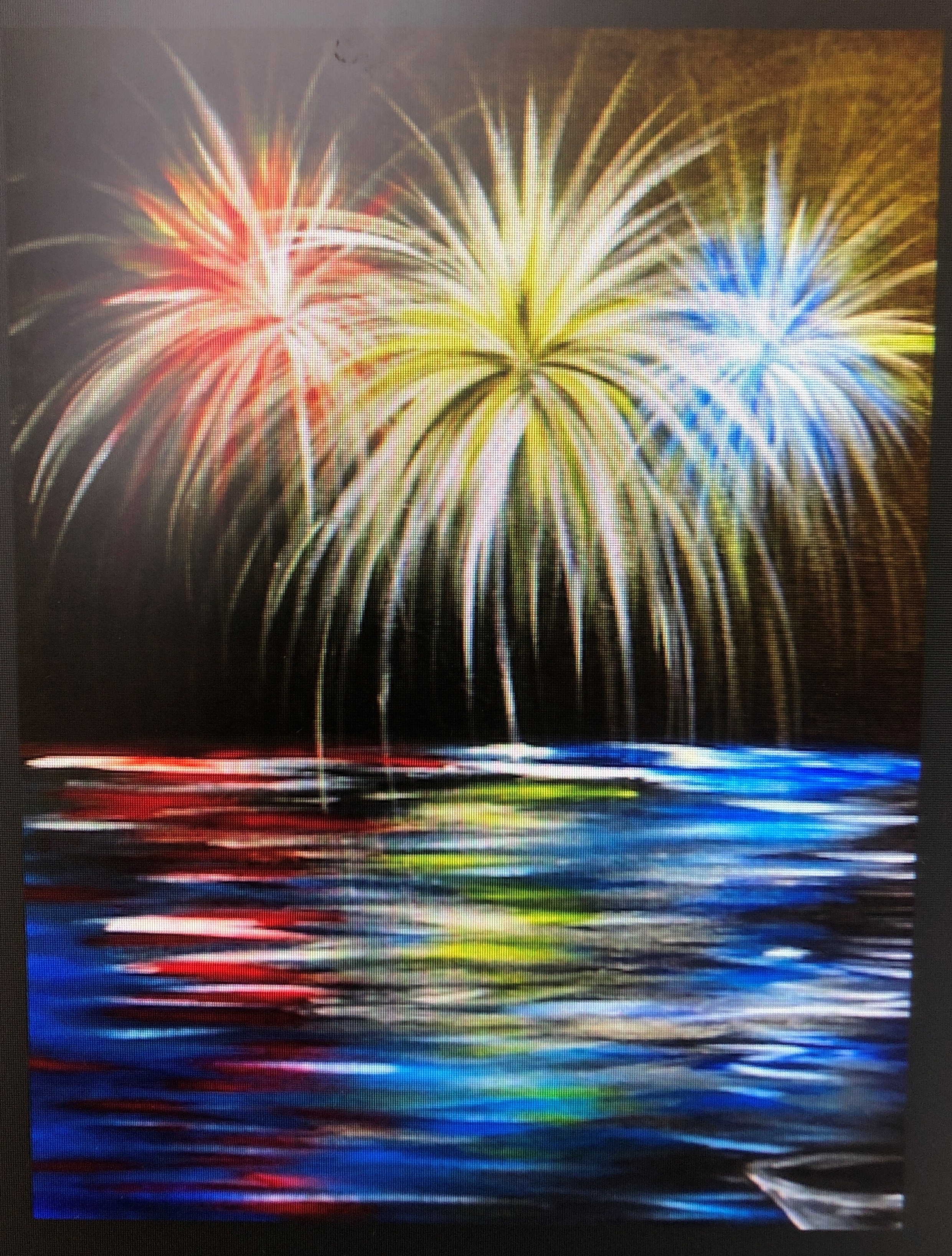 red, white, and blue fireworks over a lake with a small white boat on a black canvas