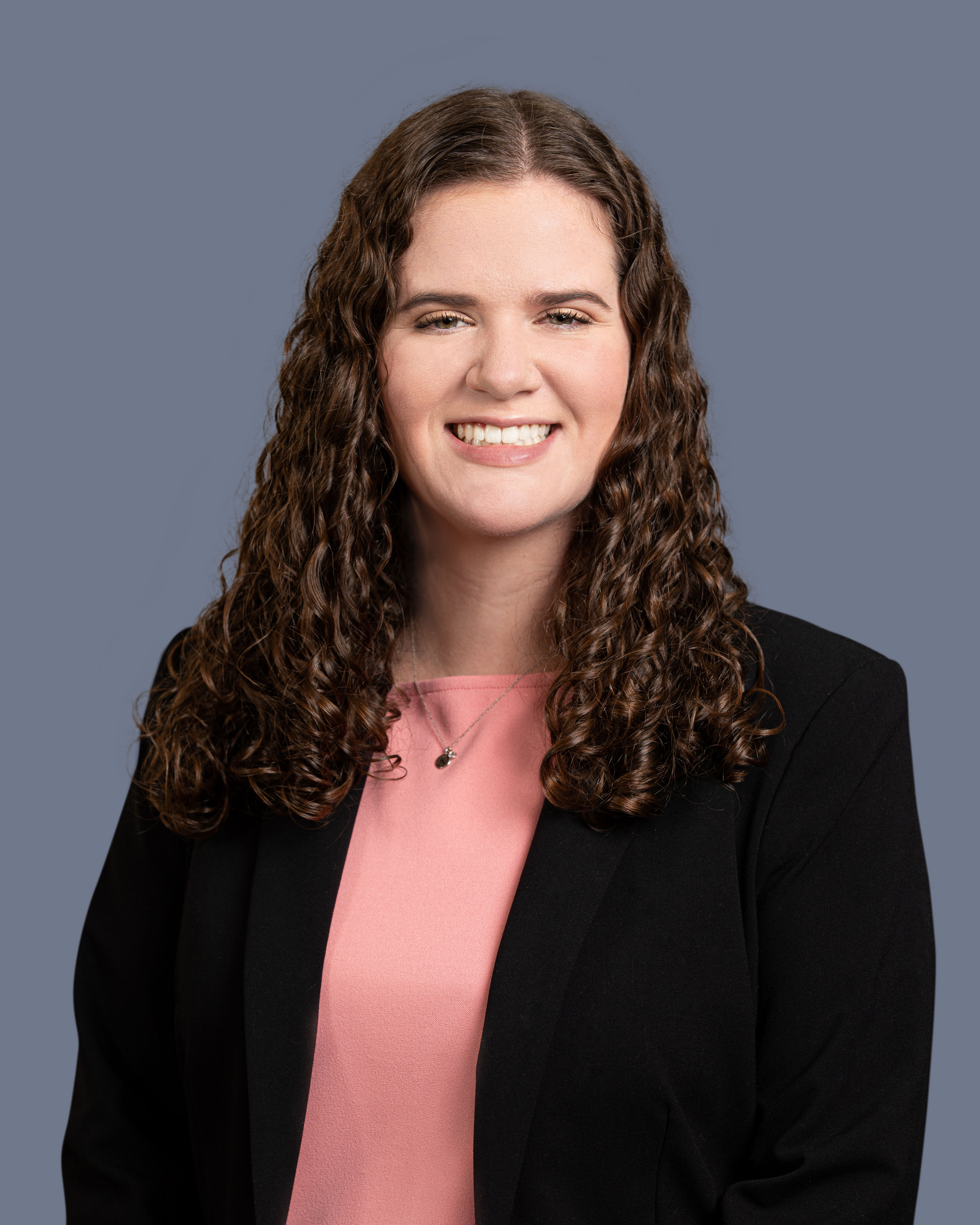 Headshot of woman with curly brown hair, pink shirt, and black jacket.