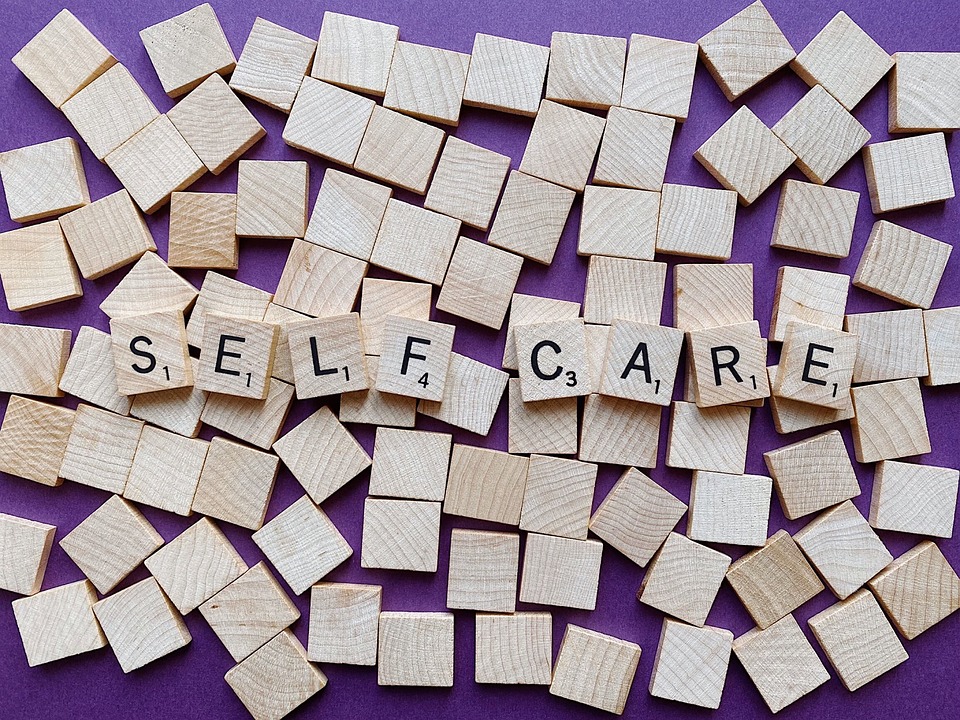 self care written in scrabble tiles on top of a scattering of wooden tiles with a purple background