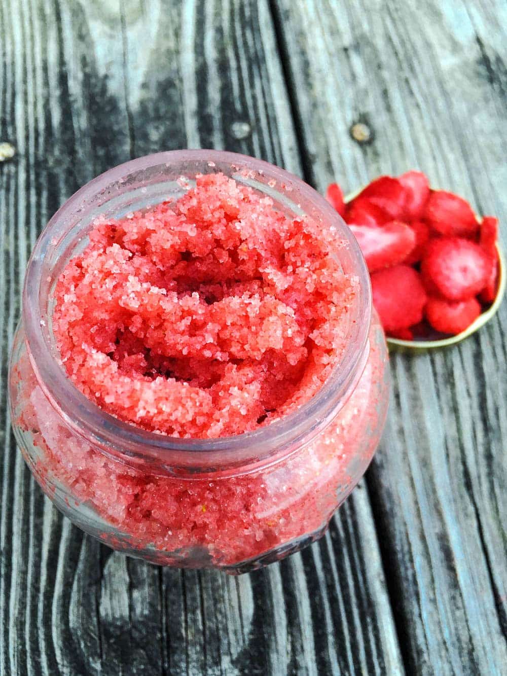 a close up picture of the sugar scrub in a car with a blurred background of strawberries and distressed wood