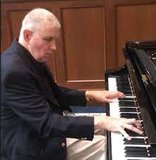 A man playing a piano with white hair.