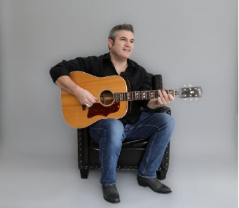Steve Dunn sitting, playing a guitar against a gray background.