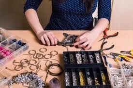 Jewelry making supplies on a table with a beading and tools. In the middle, there are two hands making a project. 