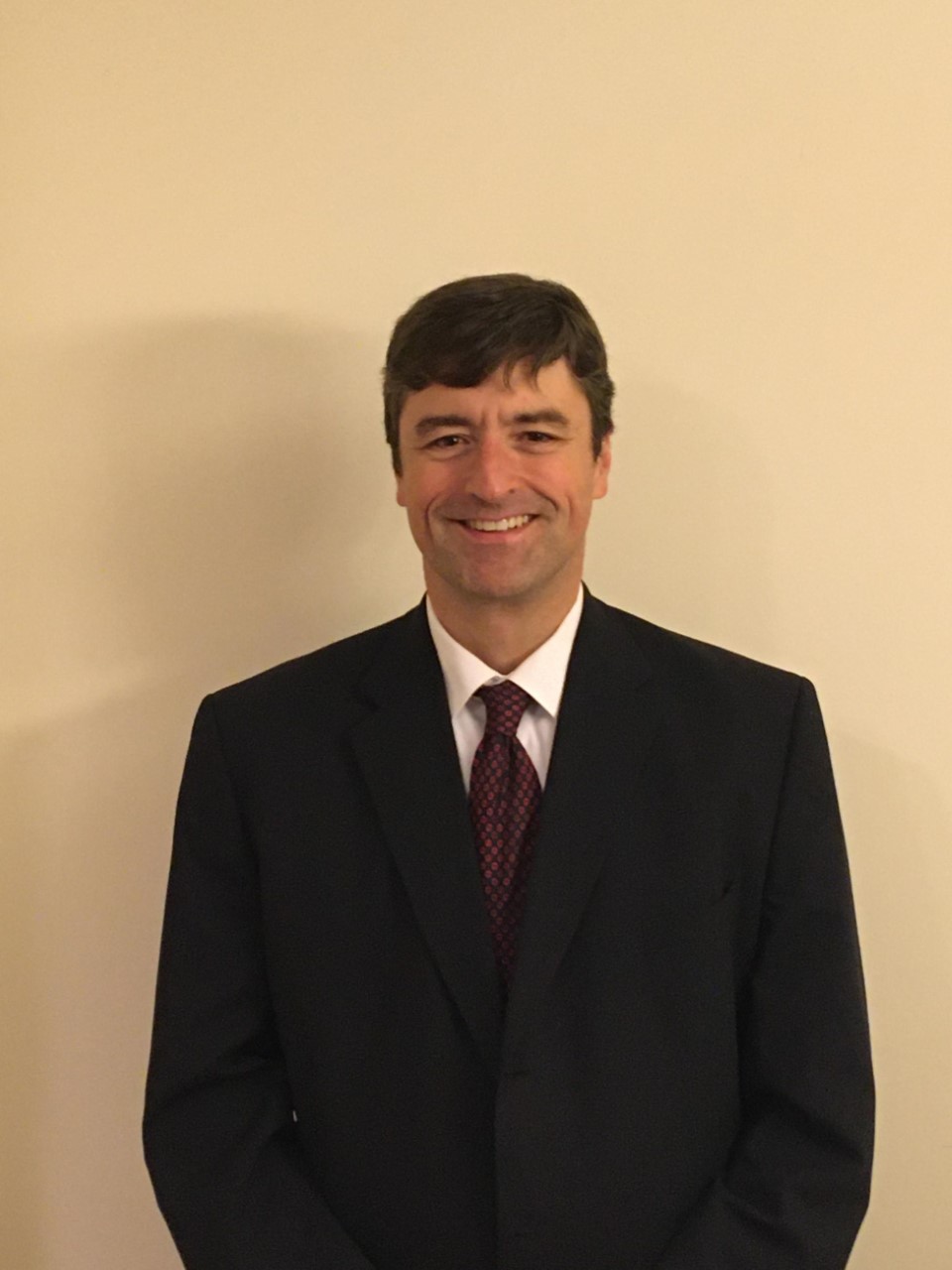 A person standing in front a beige background.