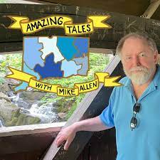 A man standing next to a wooden opening that overlooks a small waterfall. Displayed is the Amazing Tales Logo with a simplified version of Connecticut in various tones of blue.  