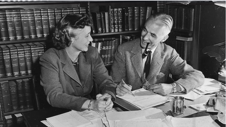 black and white photograph of a Lewis Walpole and a woman sitting in a library, talking and smiling. 