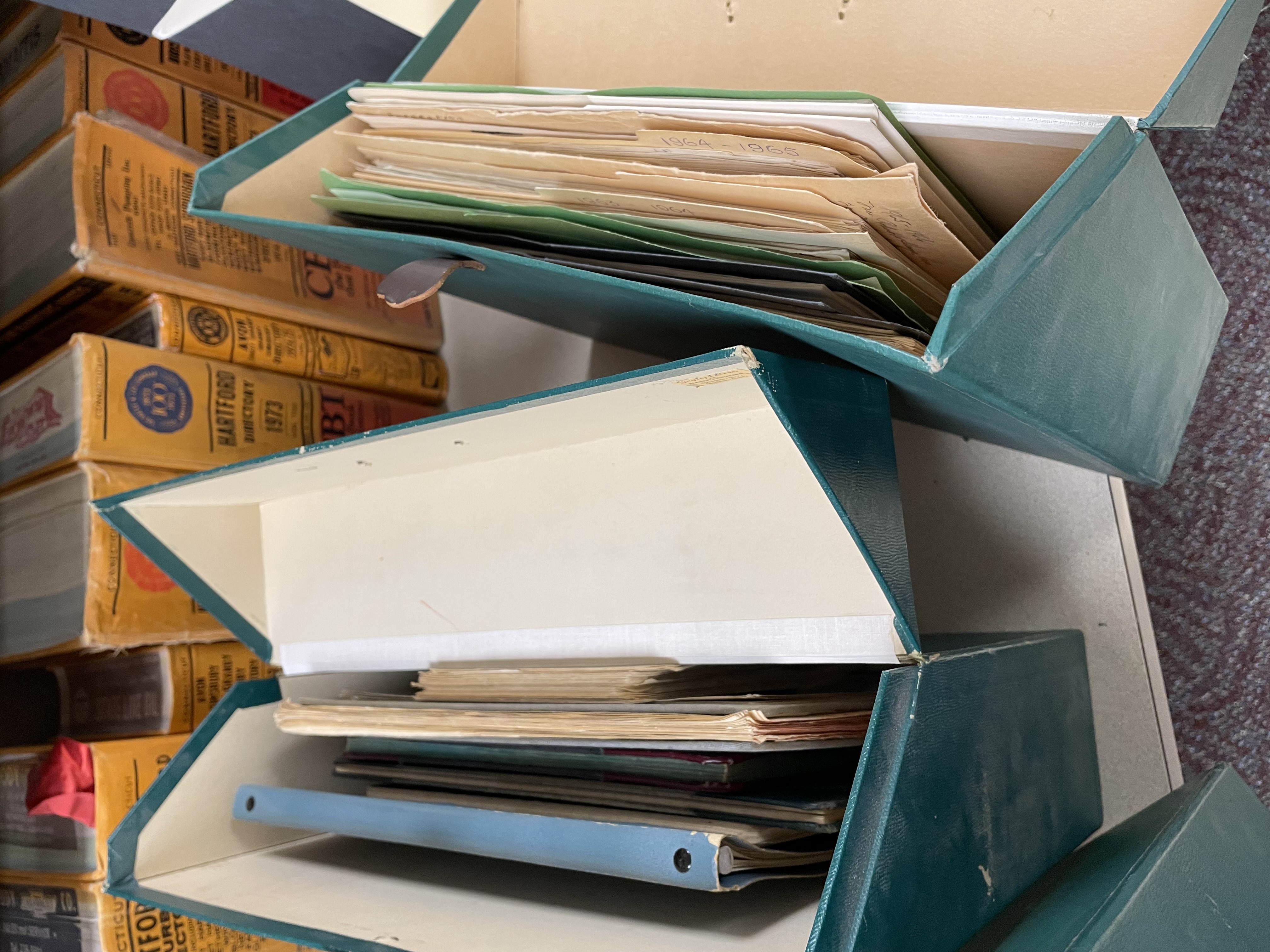 : Three green archival boxes with leather tabs on a counter. One has two labels attached: “Farmington Valley Woman’s Club” and “Farmington Valley Woman’s Club: Year Books; Community Affairs Book; Dr. Dunne Scholarship Book & Award.”