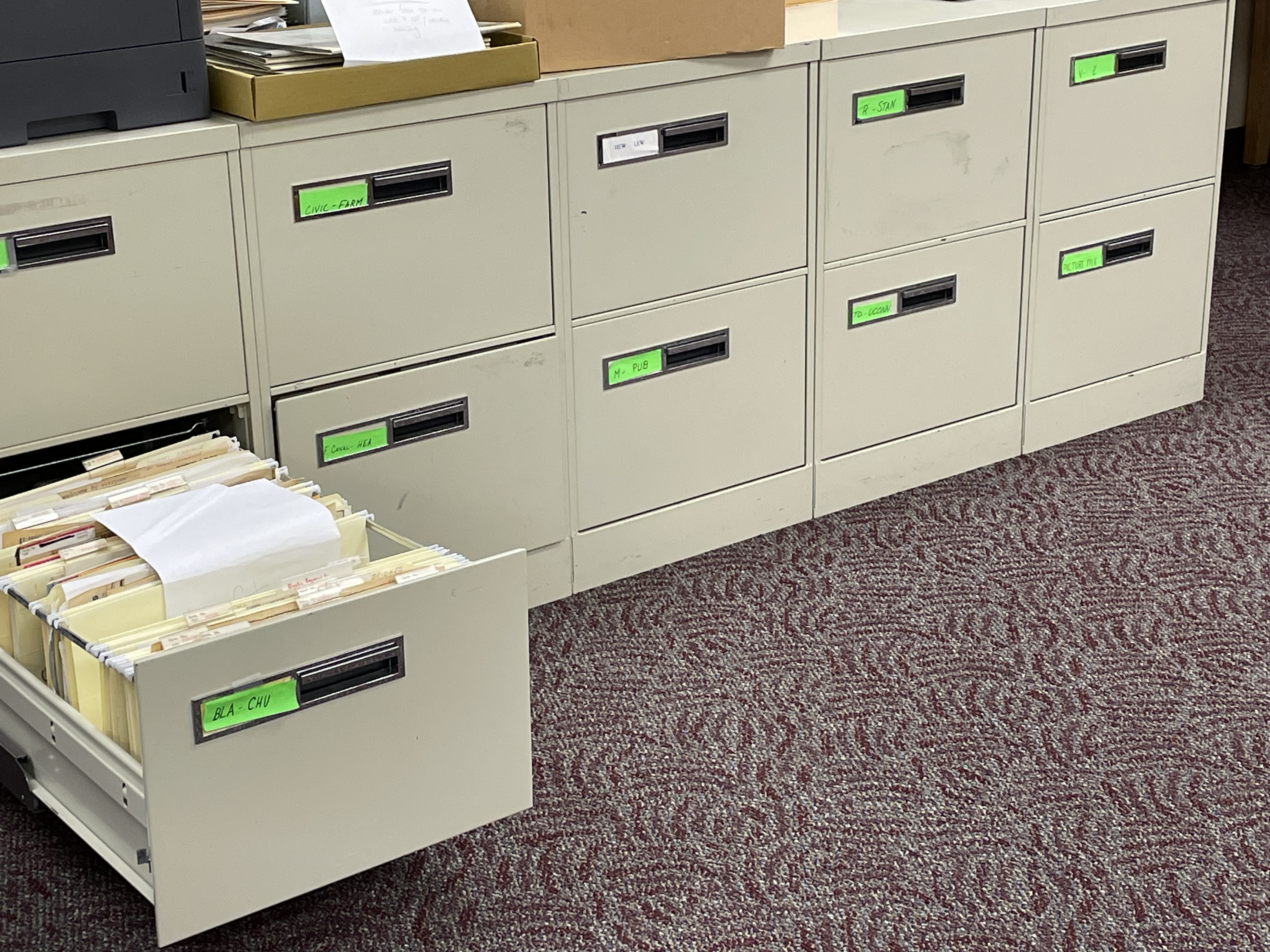 A large, low filing cabinet running along a wall. One drawer has been pulled out to show the files inside.