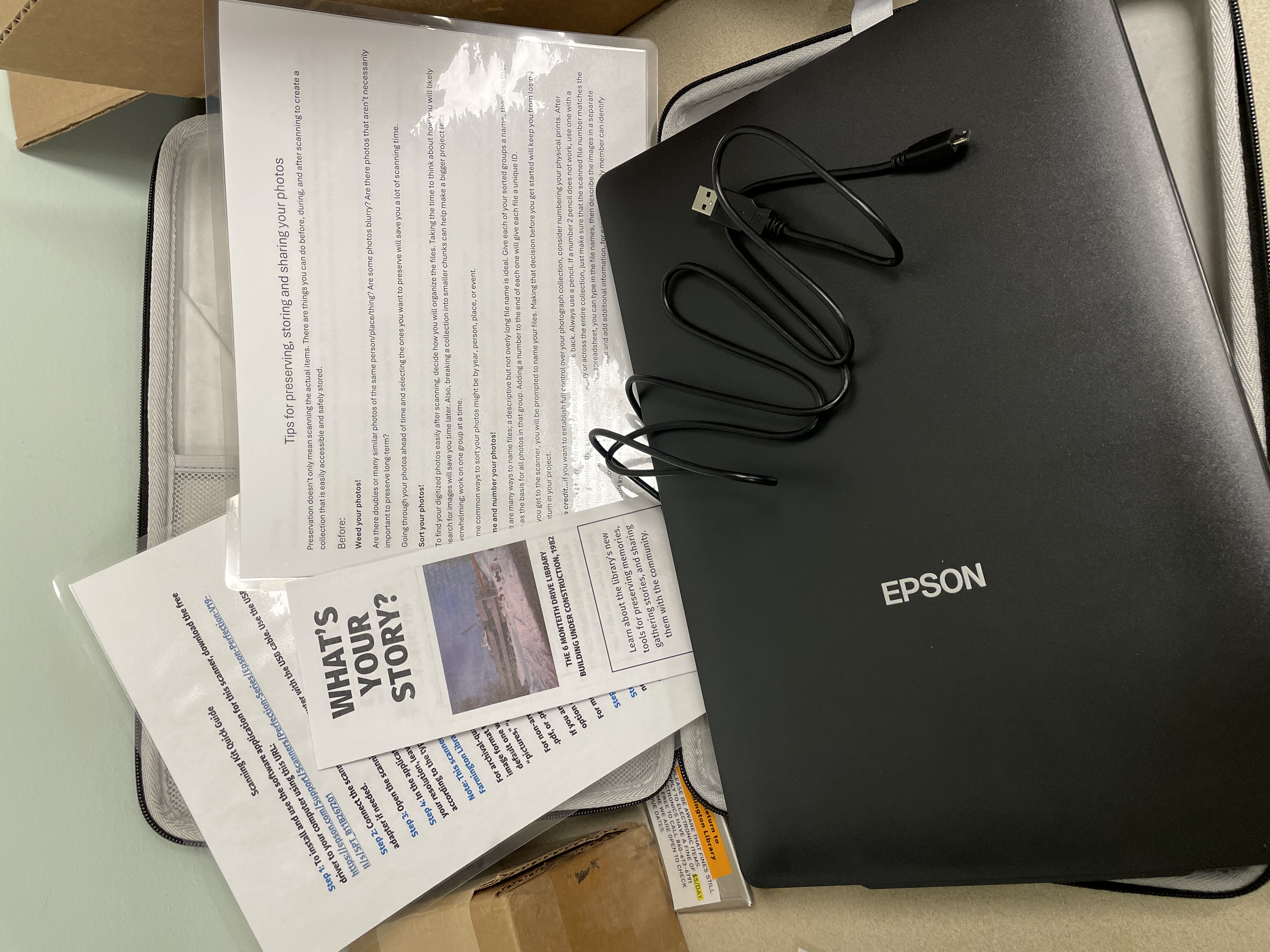 An open case on a table with an Epson flatbed scanner and several laminated guides.