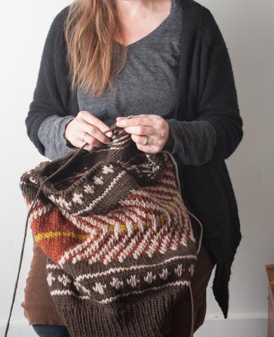 a person knitting a complex patterned project that has brown, white, and yellow stiching
