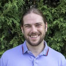 a man in a blue collared polo shirt against a greenery background