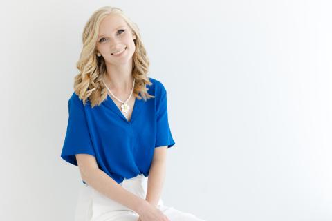 A headshot of Elizabeth Hester in a blue blouse and white pants against a white background