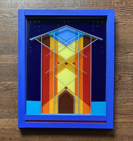Framed geometric artwork featuring vibrant colors, including blue, yellow, red, and orange, arranged in a symmetrical, abstract pattern resembling a stylized architectural structure. The frame is painted bright blue, contrasting with the rich, colorful composition.