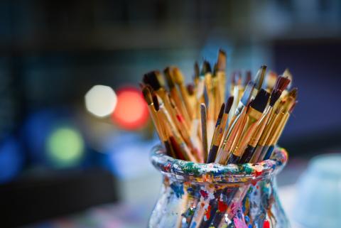 a photo of multiple used paintbrushes in a jar against a blurred background with lights in green yellow and red