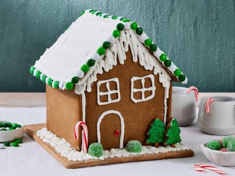 a amateur gingerbread house with frosting and candy decorations against a background of dark greyblue on a white table 
