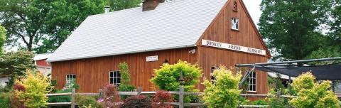 A photo of the Broken Arrow Nursery which is large wooden building that has a gray roof and a sign that says Broken Arrow Nursery on the top of it