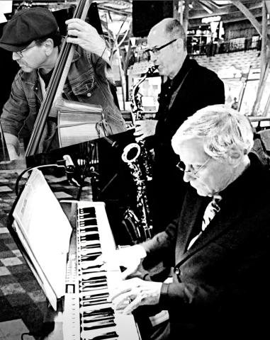 a black and white image of one man playing piano, one person playing a saxophone, and one person that has been edited in playing a bass guitar.