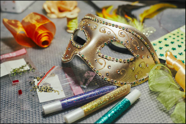 a mask on a table with crafting supplies next to it. It is carnival/mardi gras themed.