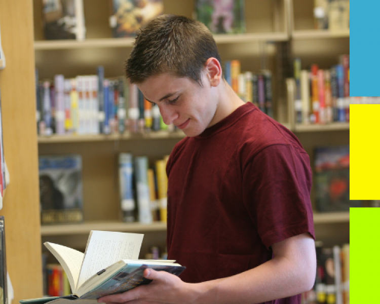 Teen boy reading book in library
